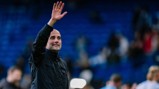 A person with a blurred face wearing a black jacket and raising their hand at a stadium with a blue seating background.