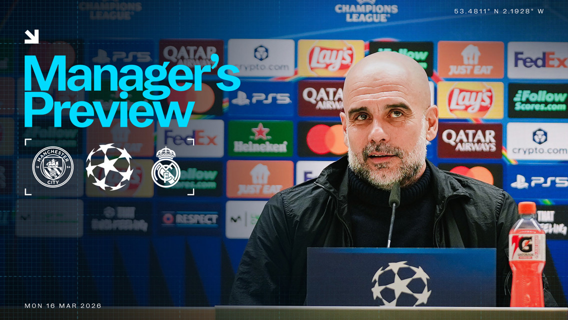 An image showing a blurred manager at a press conference for the UEFA Champions League match between Manchester City and Real Madrid, with logos and sponsor banners in the background.