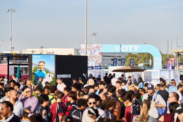 Crowd gathered at a Manchester City event with visible signs displaying 'CITY' and 'Number 10'.