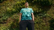 Person wearing a Manchester City shirt with a hexagonal pattern, standing against a wall of greenery.
