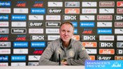 A man in a grey jacket sits at a press conference table with microphones, in front of a backdrop of sponsor logos, including Manchester City Logo and Barclays WSL.