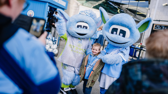 A child poses with two blue mascots outside the Manchester City merchandise store.