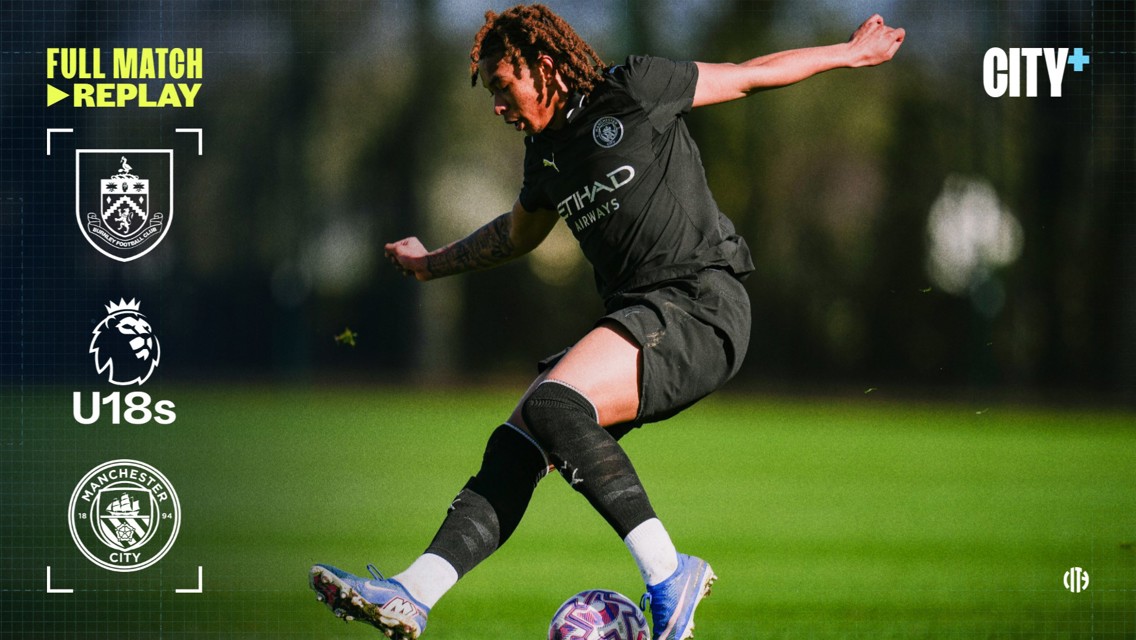 Blurred image of a U18 soccer player in black Manchester City kit kicking the ball during a match against Burnley, logos of clubs and Premier League U18s visible.