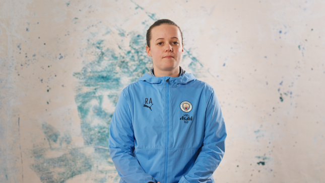 Person in a blue Manchester City jacket with Puma and 'RA' initials, standing against a marbled background.
