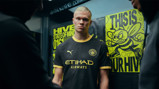 A person wearing a black Manchester City uniform with yellow accents stands in front of posters featuring a bee and text: 'Hive' and 'State of Mind'.