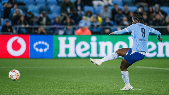A football player wearing jersey number 9 attempts a goal in a stadium, with Heineken and Vodafone ads visible in the background.