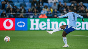 A football player wearing jersey number 9 attempts a goal in a stadium, with Heineken and Vodafone ads visible in the background.