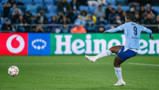 A football player wearing jersey number 9 attempts a goal in a stadium, with Heineken and Vodafone ads visible in the background.
