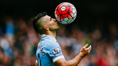 A soccer player in a Manchester City jersey heads a ball during a match.
