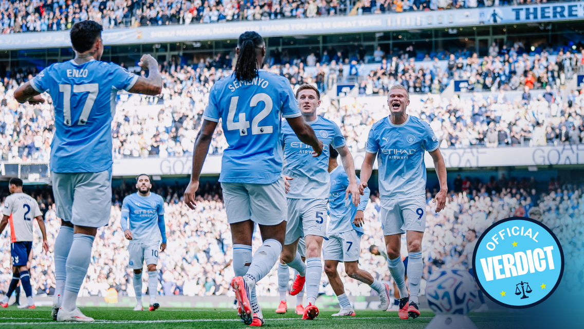 Manchester City players celebrating a goal at Etihad Stadium, wearing light blue kits with crowd in background.