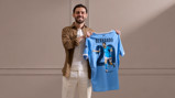 A person holds a Manchester City jersey featuring the name 'Bernardo' and number 20 with a cartoon illustration.