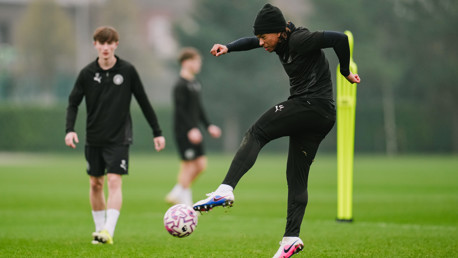Athletes on a soccer field during a training session, with one player actively controlling a ball.