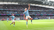 Manchester City player in blue jersey celebrates a goal at Etihad Stadium with enthusiastic crowd in the background.