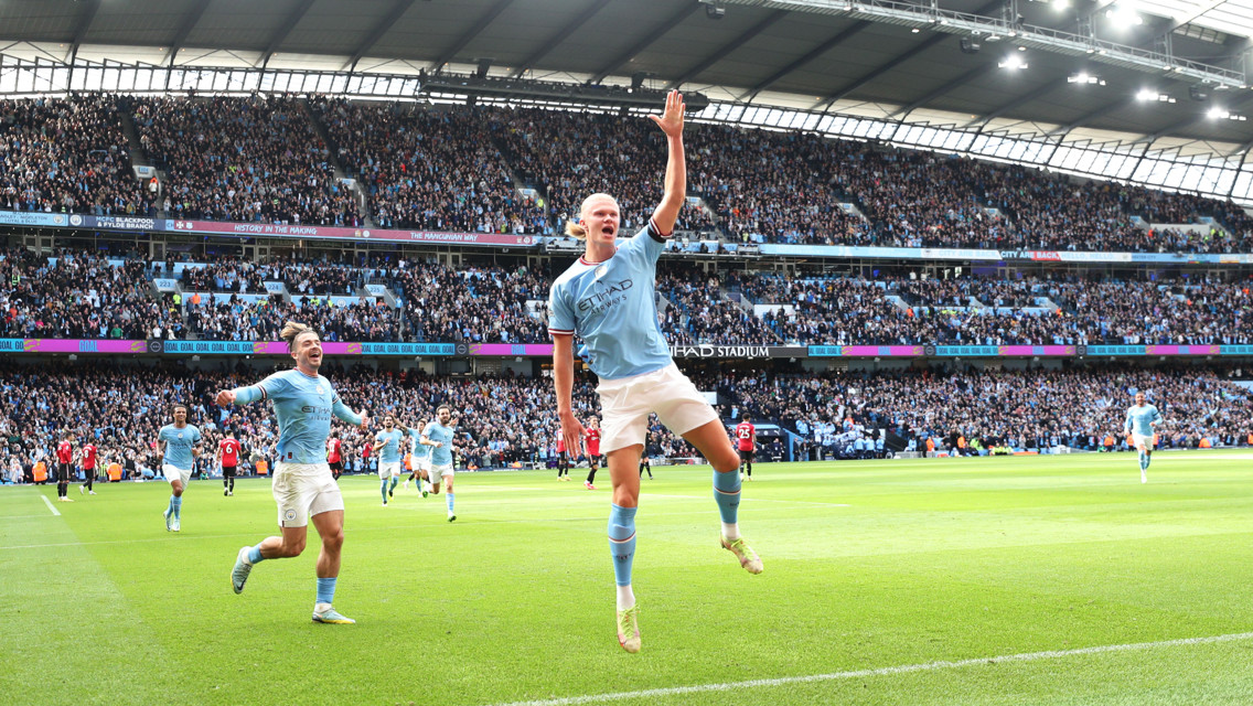 Manchester City player in blue jersey celebrates a goal at Etihad Stadium with enthusiastic crowd in the background.