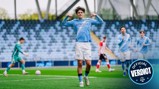 A football player wearing a Manchester City jersey celebrates a goal with his arms flexed. Other players and a goalkeeper are visible on the pitch with empty stands in the background. An 'Official Verdict' badge is in the bottom right corner.