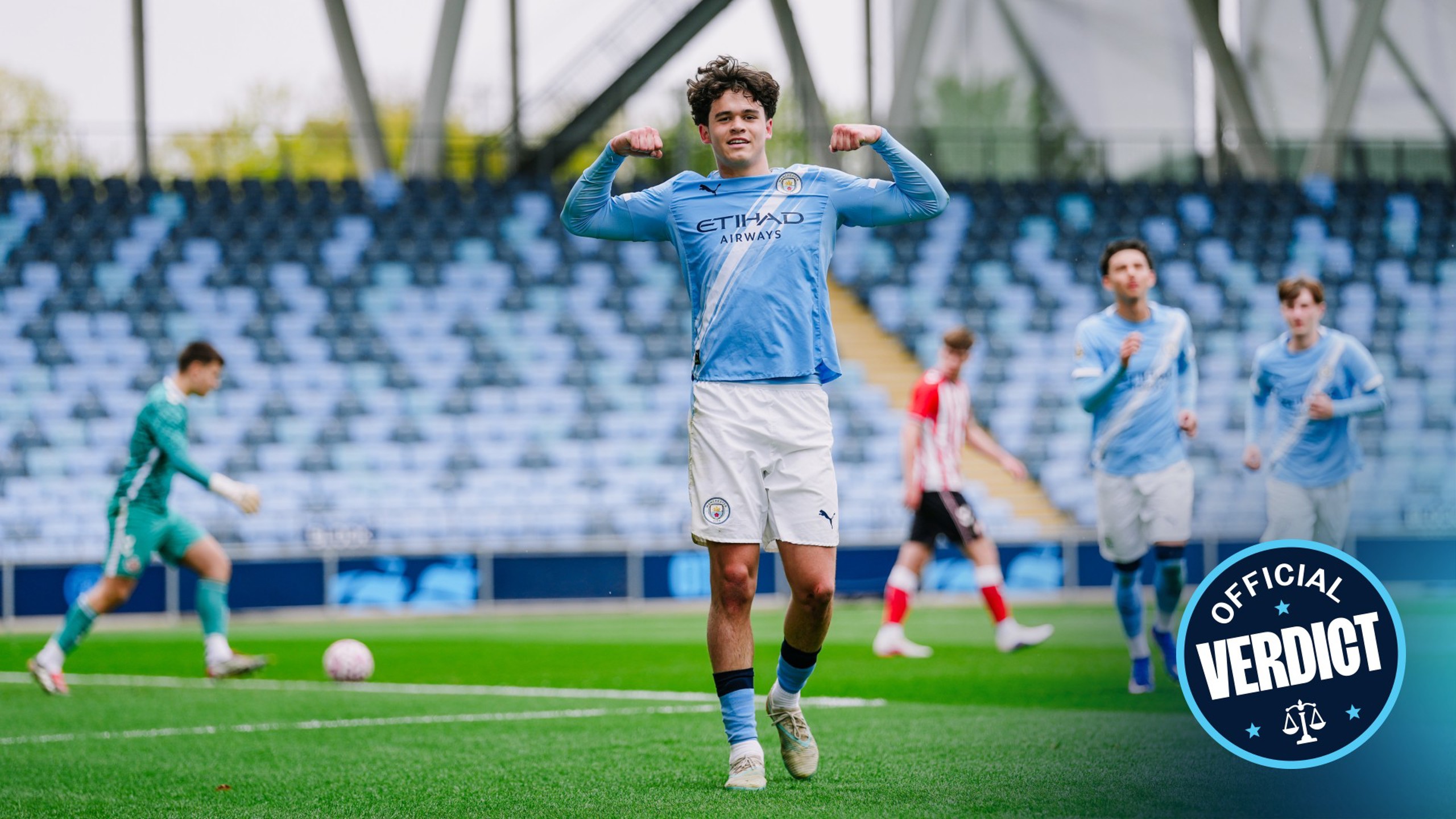A football player wearing a Manchester City jersey celebrates a goal with his arms flexed. Other players and a goalkeeper are visible on the pitch with empty stands in the background. An 'Official Verdict' badge is in the bottom right corner.