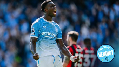 A soccer player in a Manchester City jersey celebrating a goal with clenched fists and a loud cheer on the field.