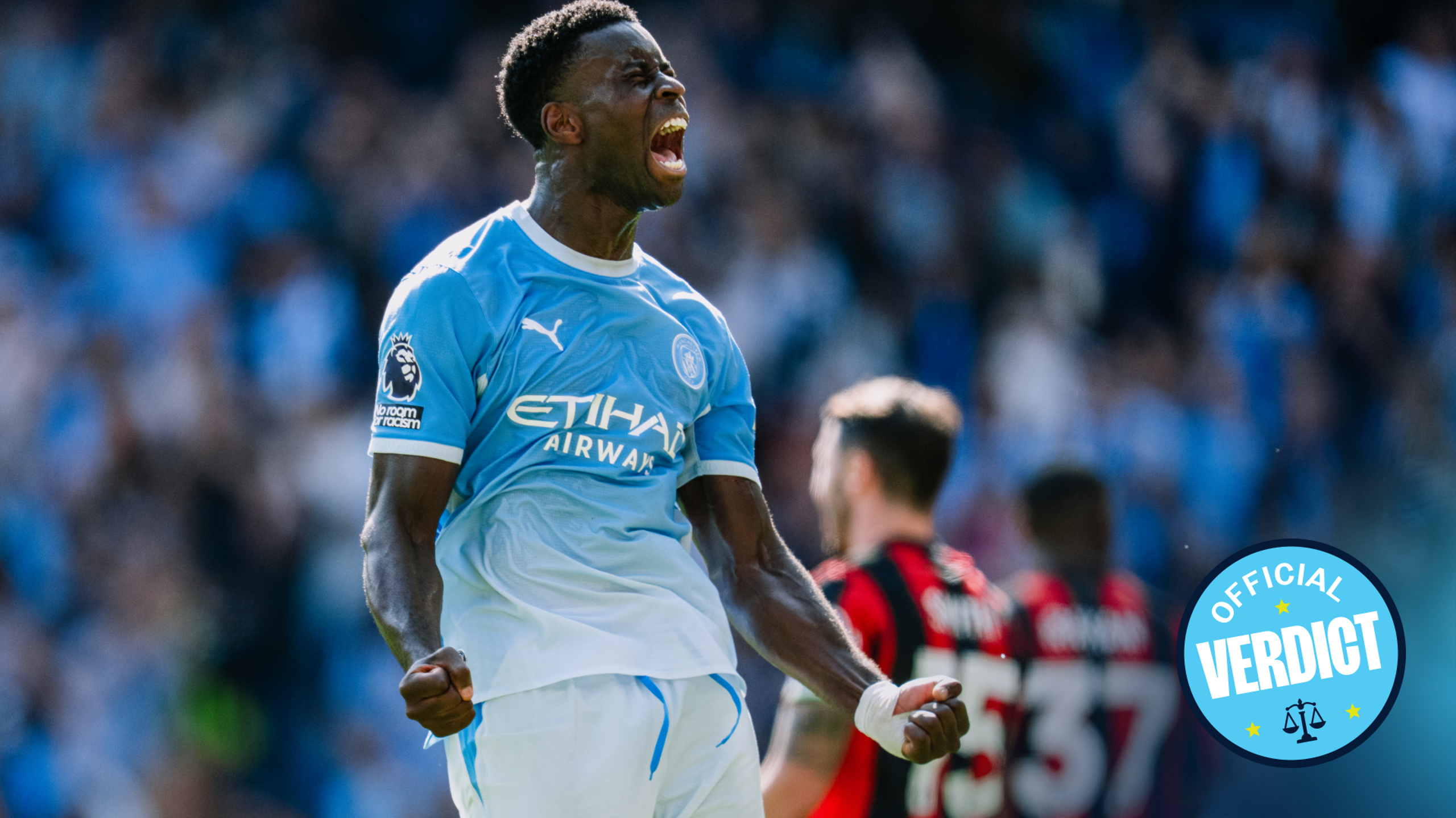 A soccer player in a Manchester City jersey celebrating a goal with clenched fists and a loud cheer on the field.