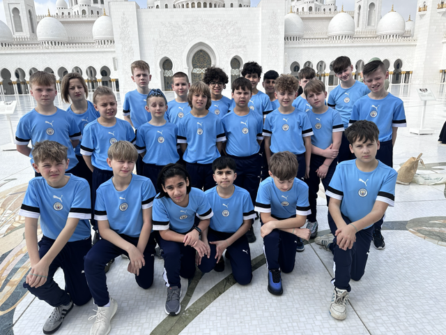 A group of kids in Manchester City shirts pose for a team photo at the Sheikh Zayed Grand Mosque.