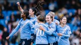 Group of Manchester City women's team players celebrating a goal on the field wearing blue jerseys.