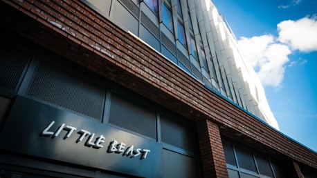 Upward view of a building exterior featuring 'Little Beast' signage, with a blue sky and clouds in the background.