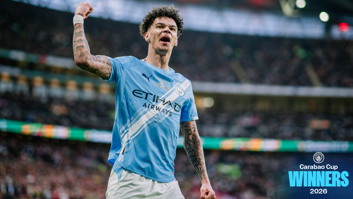 Blurred image of a Manchester City football player celebrating with arm raised. 'Carabao Cup Winners 2026' text visible on the right.