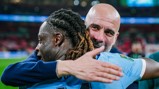Two football players embrace on the field wearing blue jerseys after a match.