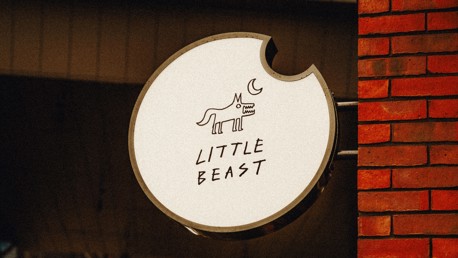 A circular sign mounted on a brick wall reads 'Little Beast' with a stylized drawing of a creature and a crescent moon.