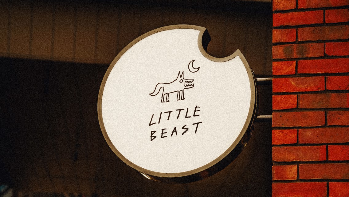 A circular sign mounted on a brick wall reads 'Little Beast' with a stylized drawing of a creature and a crescent moon.