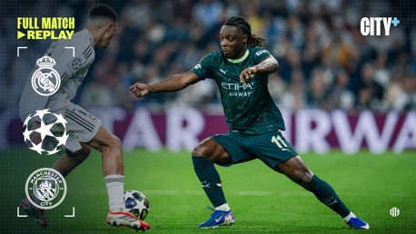 Two footballers from Real Madrid and Manchester City compete for the ball during a match. The Manchester City player is wearing a dark green kit, and the Real Madrid player is in a white kit. The image is a promotional graphic for a full match replay.