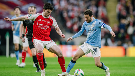 Two soccer players from Arsenal and Manchester City competing for the ball on the field.