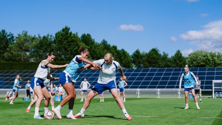 A women's soccer training session with players engaged in drills on a grass field.