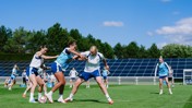 A women's soccer training session with players engaged in drills on a grass field.