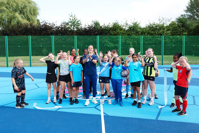 A group of young female soccer players posing on a blue sports court, wearing various sports kits.