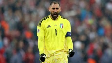 An Italian goalkeeper in a yellow kit celebrates during a match, wearing gloves and a captain's armband.