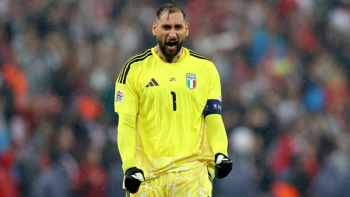 An Italian goalkeeper in a yellow kit celebrates during a match, wearing gloves and a captain's armband.