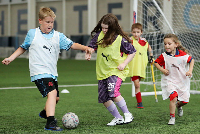 Children playing soccer on a field. Two kids in the foreground are contesting for the ball while two others are running towards them.