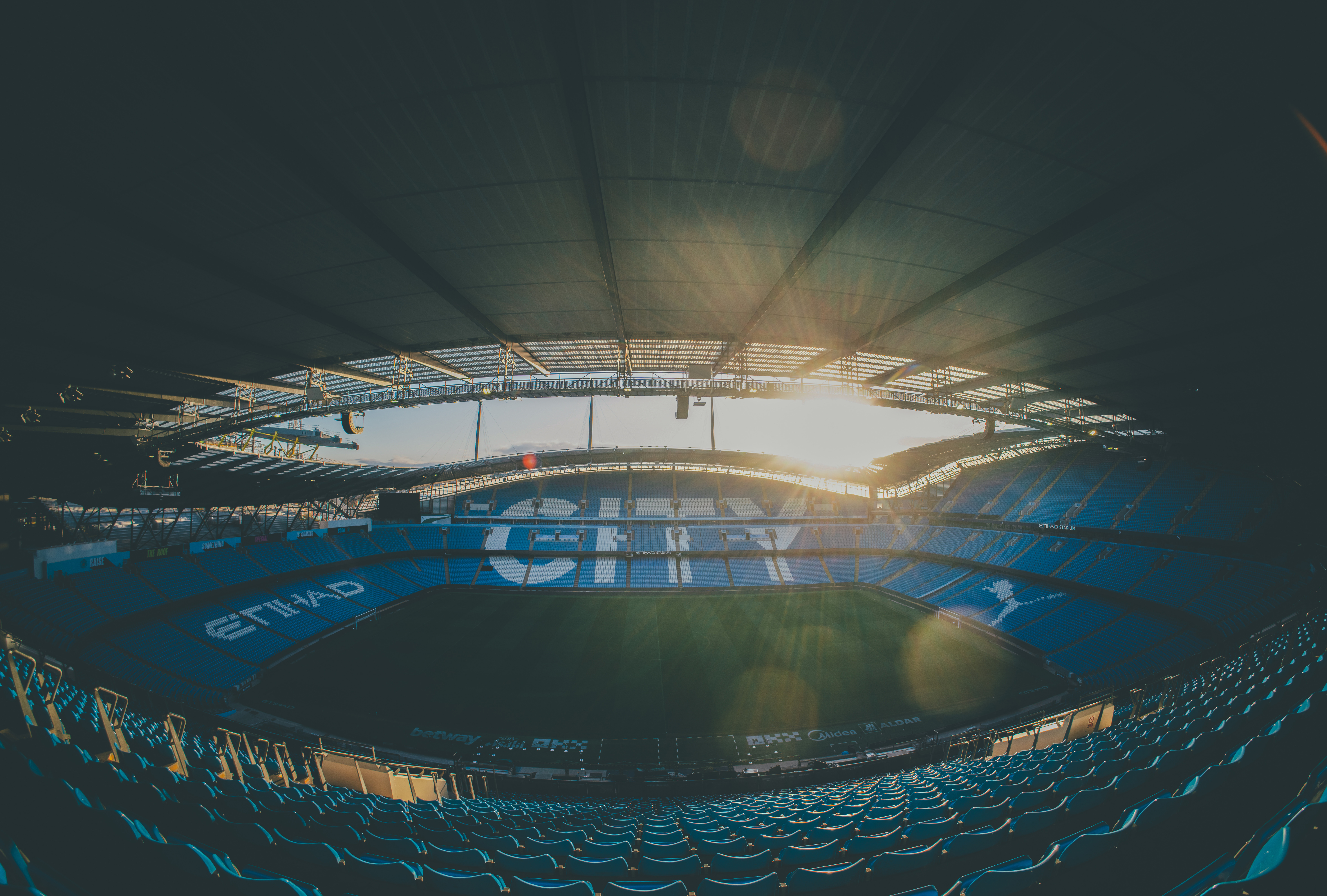 View of a stadium with blue seating and sunlight streaming through the roof.