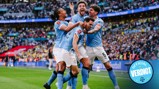 Manchester City players celebrating a goal during a football match at Wembley Stadium with a crowd in the background and an 'Official Verdict' badge visible.