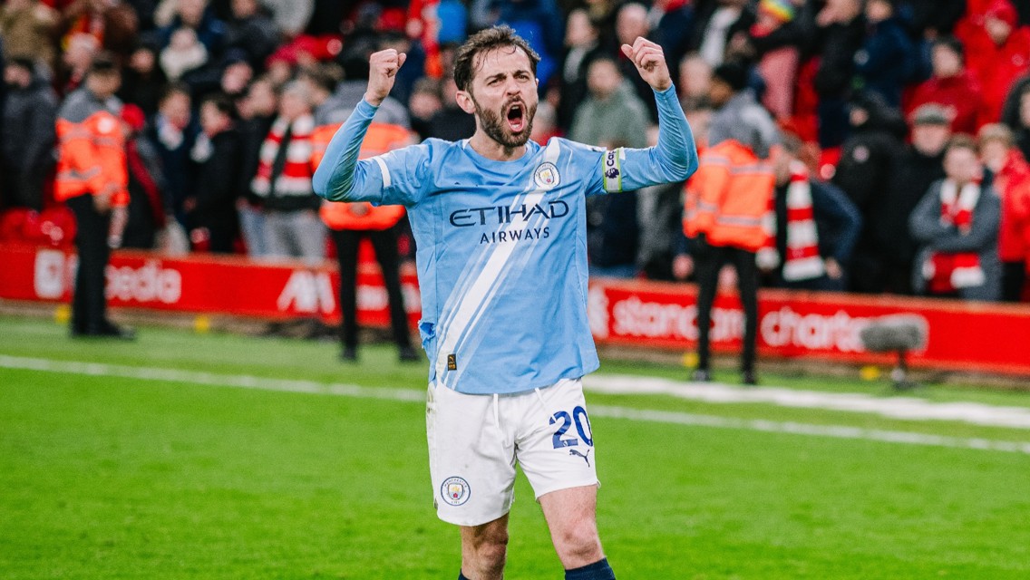 Soccer player in Manchester City kit celebrating on a football field with a crowd in the background.