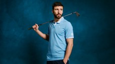 A person wearing a light blue Puma shirt holding a golf club over their shoulder against a blue background.