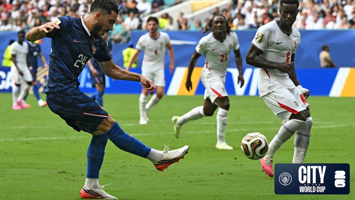 Football players in action during a World Cup match, one player kicking the ball surrounded by others, including those from opposing team.