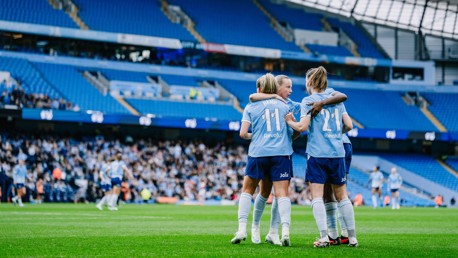 Football players in light blue jerseys celebrating on the field at a large stadium with mostly empty seats.