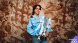 A woman wearing a Manchester City football jersey holding a silver Barclays trophy against a textured brown background.