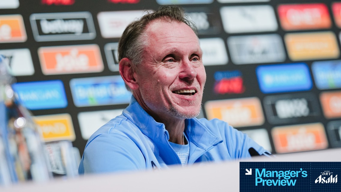 A blurred portrait of a person at a press conference with 'Manager's Preview' and 'Asahi Super Dry' logos.