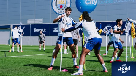 Players training at Manchester City's City Football Academy. They are interacting with training poles, dressed in team gear, with the club's branding visible.