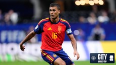 A football player wearing a red and blue Spanish jersey with the number 16 is in action during a World Cup match. The stadium background features blurry spectators.