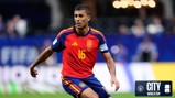 A football player wearing a red and blue Spanish jersey with the number 16 is in action during a World Cup match. The stadium background features blurry spectators.