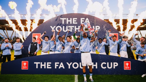 Manchester City Youth Team celebrating their FA Youth Cup victory with fireworks in the background.