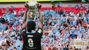 A player in a black jersey lifts a trophy in front of a cheering crowd. The jersey number is 9, and name 'Bunny' is visible. The text 'Adobe Women's FA Cup Winners 2026' is prominent.